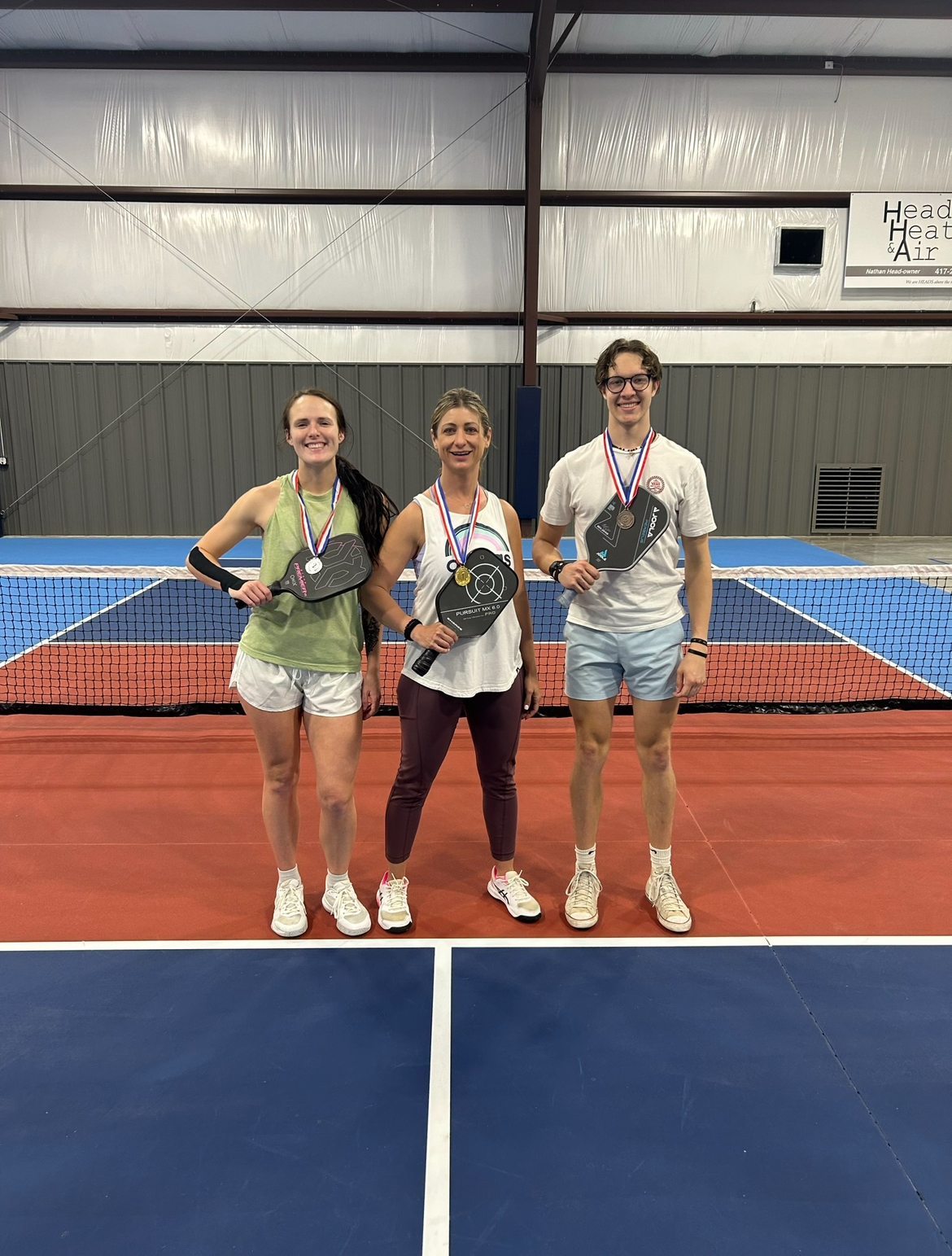 Three medalists with paddles on indoor pickleball court